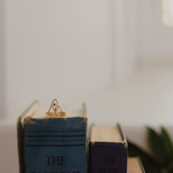 Gold Dauntless Heart ring featuring a pear-shaped aquamarine, displayed on books with soft lighting.