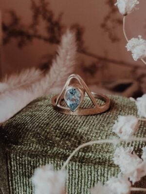 Dauntless Heart Aquamarine Ring in 14k gold on green velvet ring box with dried baby's breath, foliage, and crystal accents