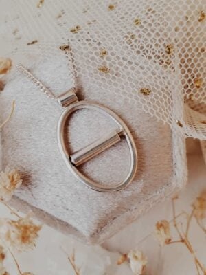 Eunoia Oval kinetic fidget necklace in sterling silver, displayed on a velvet ring box with tulle and dried florals in the background