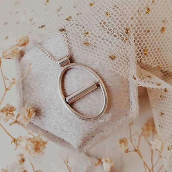 Eunoia Oval kinetic fidget necklace in sterling silver, displayed on a velvet ring box with tulle and dried florals in the background