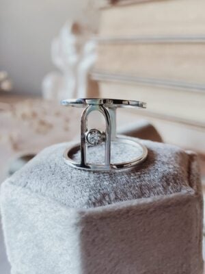 Faustina Wide Arch Statement Ring in sterling silver with central moissanite, resting on a cream velvet ring box surrounded by books and dried florals.