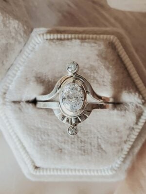 Two-band Saturn ring set in sterling silver with sapphire center stone and moissanite accents, displayed in a cream velvet ring box.