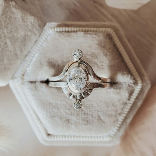 Two-band Saturn ring set in sterling silver with sapphire center stone and moissanite accents, displayed in a cream velvet ring box.