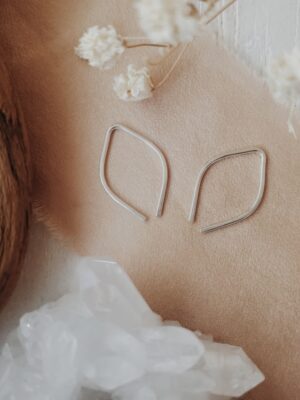 Tiny silver leaf threader earrings displayed with soft florals
