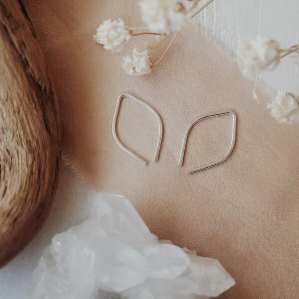 Tiny silver leaf threader earrings displayed with soft florals