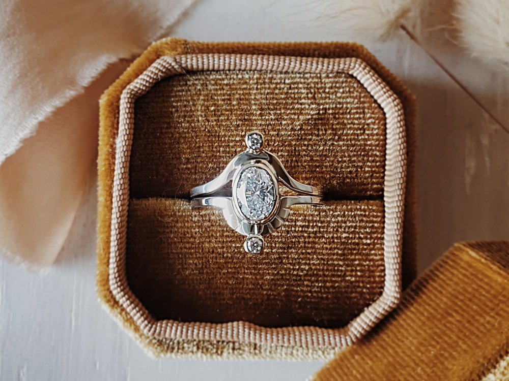 Two-band Saturn ring set in sterling silver with sapphire center stone and moissanite accents, displayed in a cream velvet ring box.