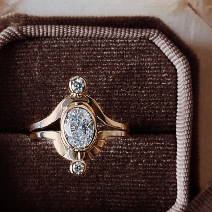 Two-band Saturn ring set in 14k gold with moissanite center stone and moissanite accents, displayed in a brown velvet ring box.