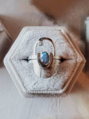 Interlocking arch ring set in sterling silver with 14k yellow gold accent, featuring oval labradorite and moissanite accent stone, displayed in velvet ring box with sage green ribbon.