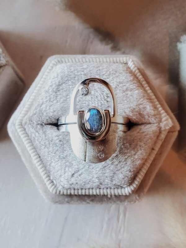 Interlocking arch ring set in sterling silver with 14k yellow gold accent, featuring oval labradorite and moissanite accent stone, displayed in velvet ring box with sage green ribbon.
